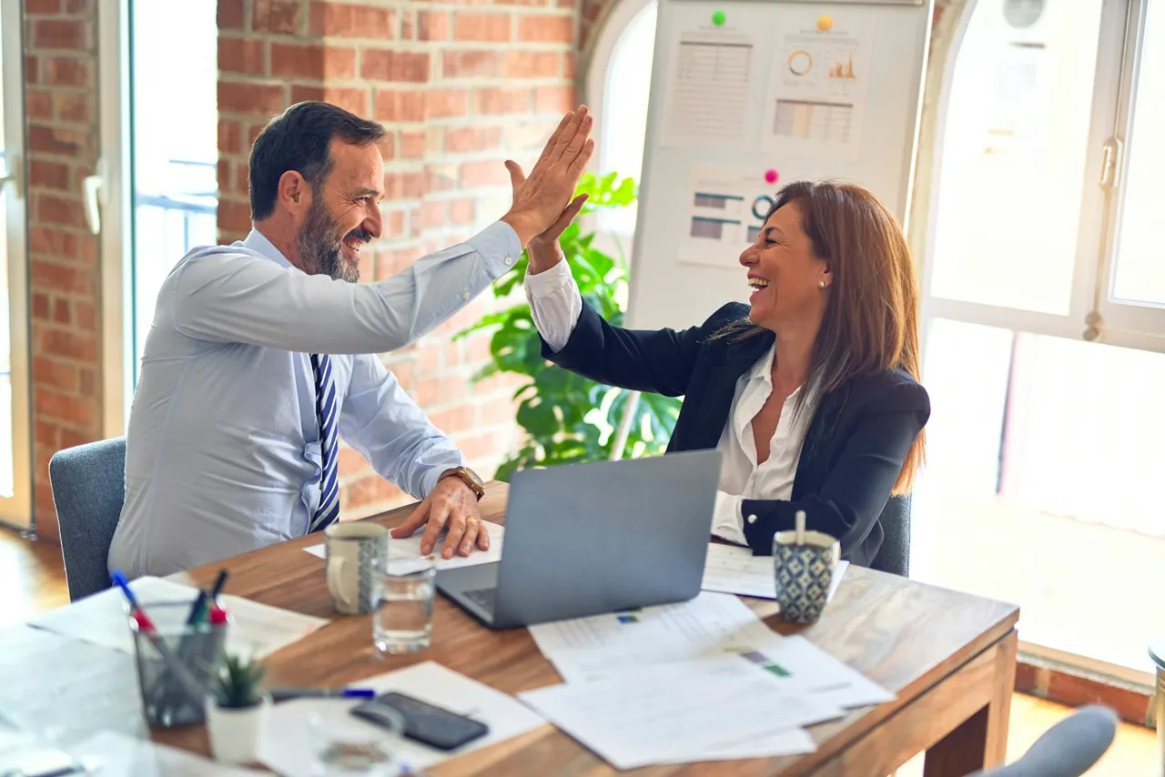 Two colleagues sharing a high-five across an office desk
